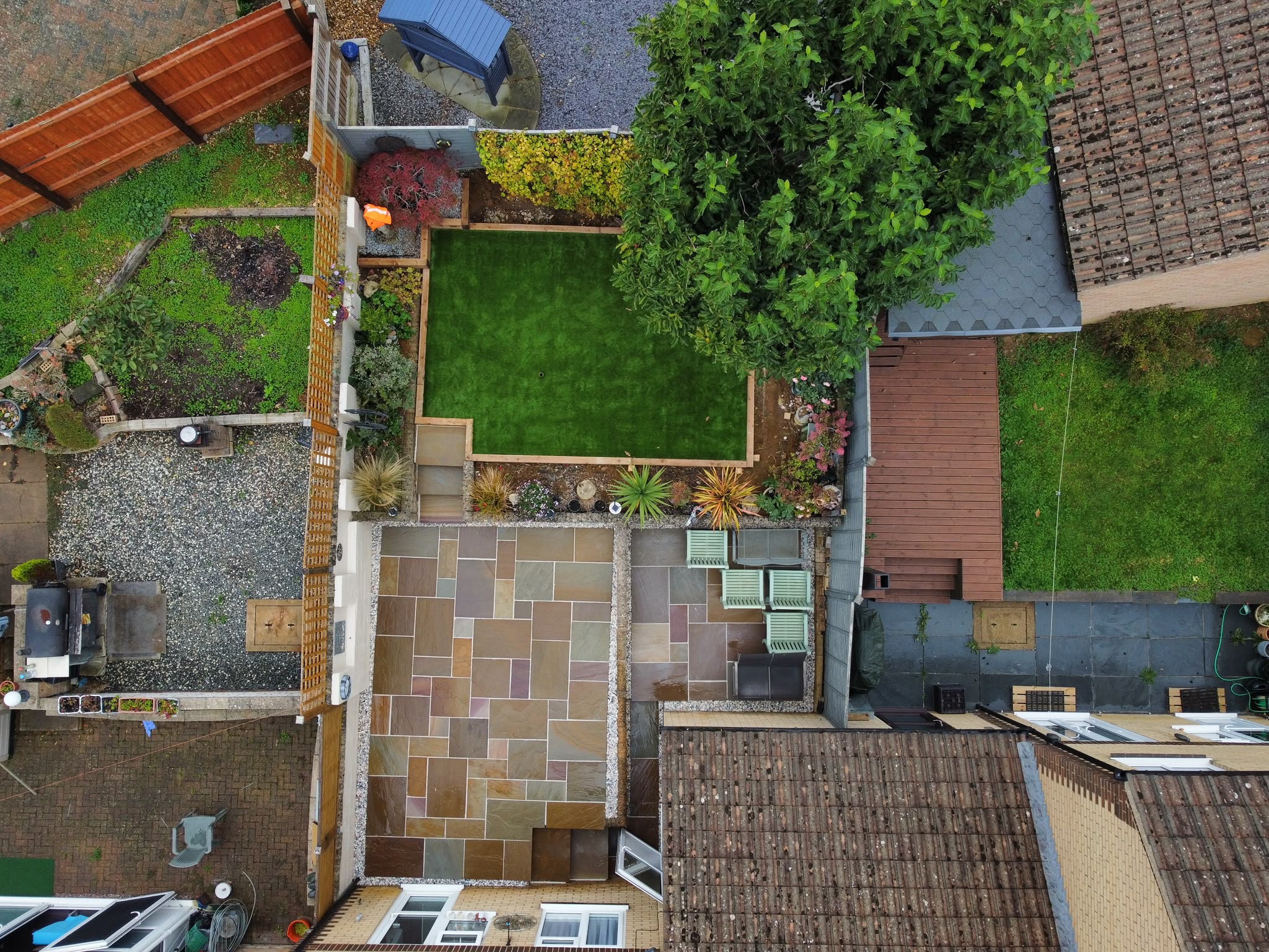 Aerial view of a finished rear garden with a sandstone patio, artificial lawn and gravel