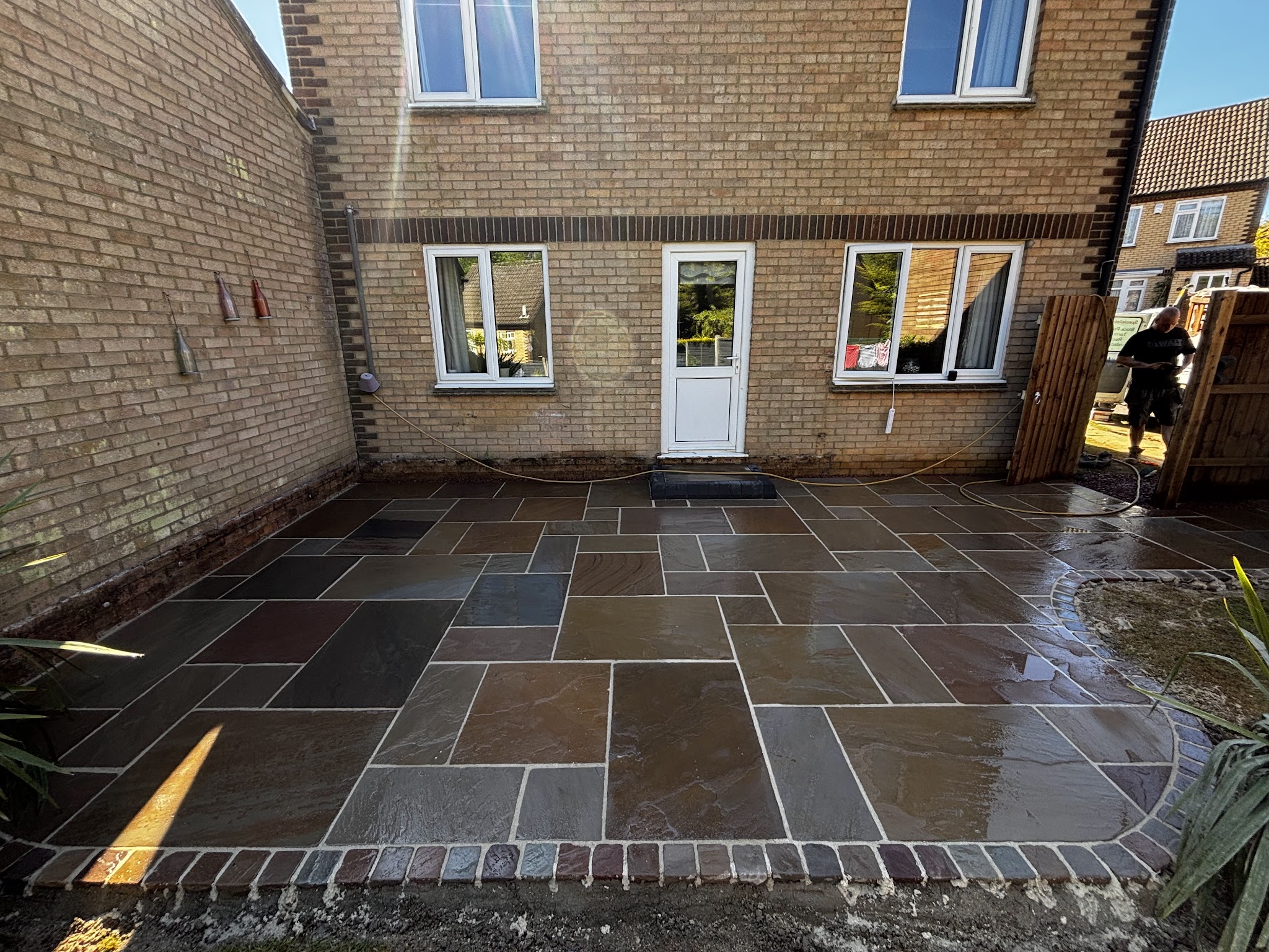 Newly laid sandstone patio with a brick-edged border behind a house