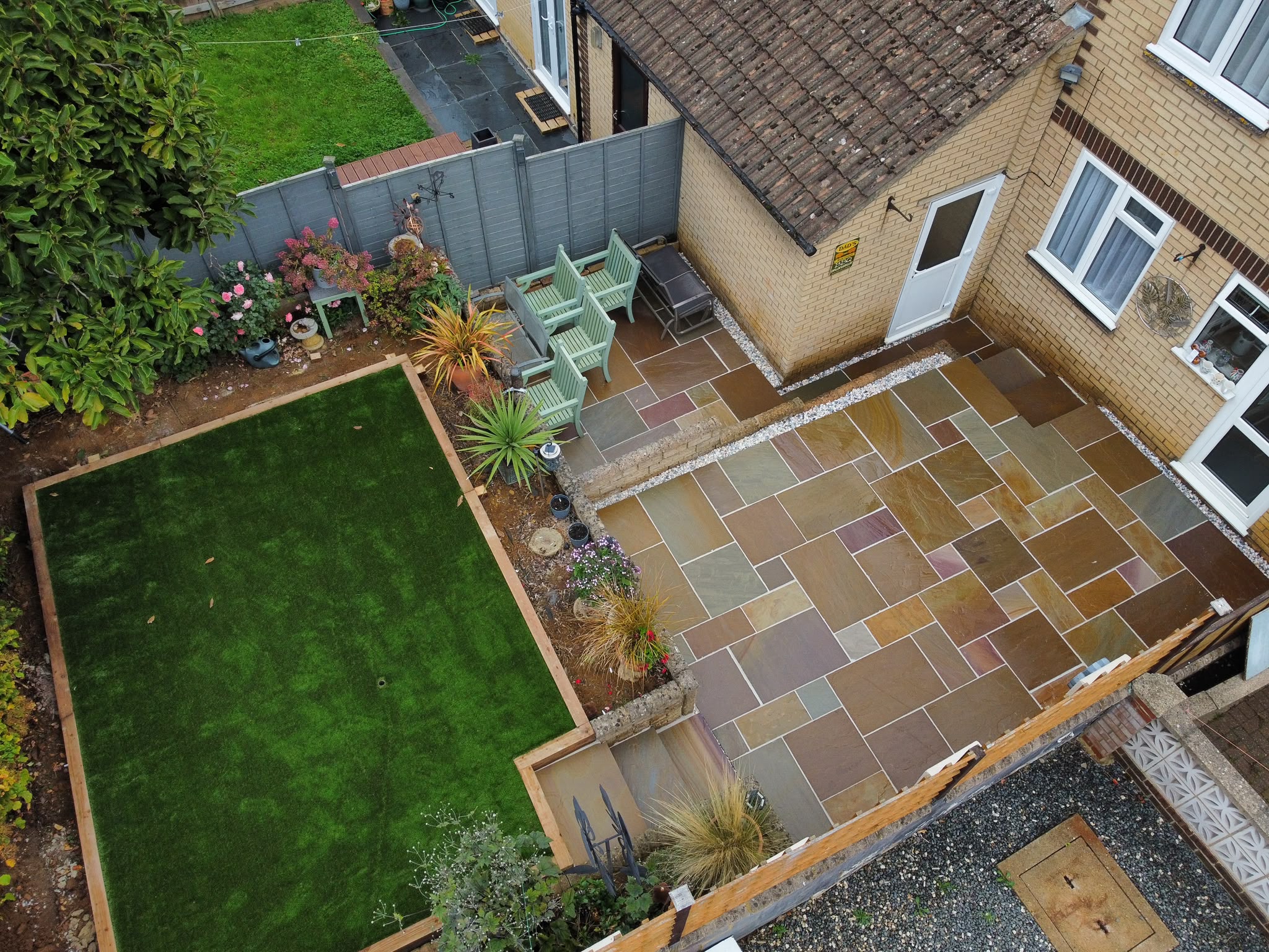 Sandstone patio beside a new artificial lawn edged with timber sleepers