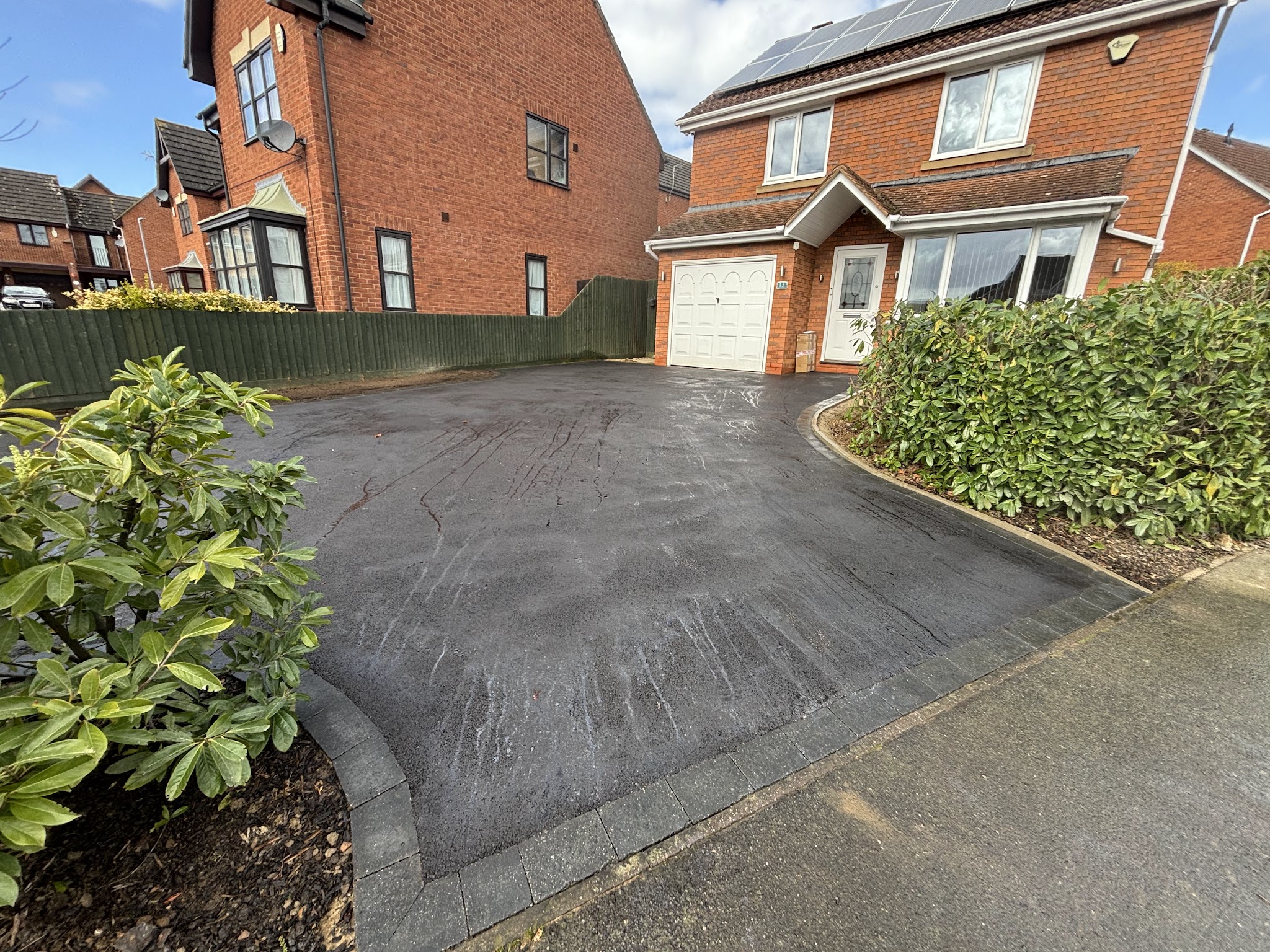 Curved tarmac driveway edged with charcoal blocks outside a detached house