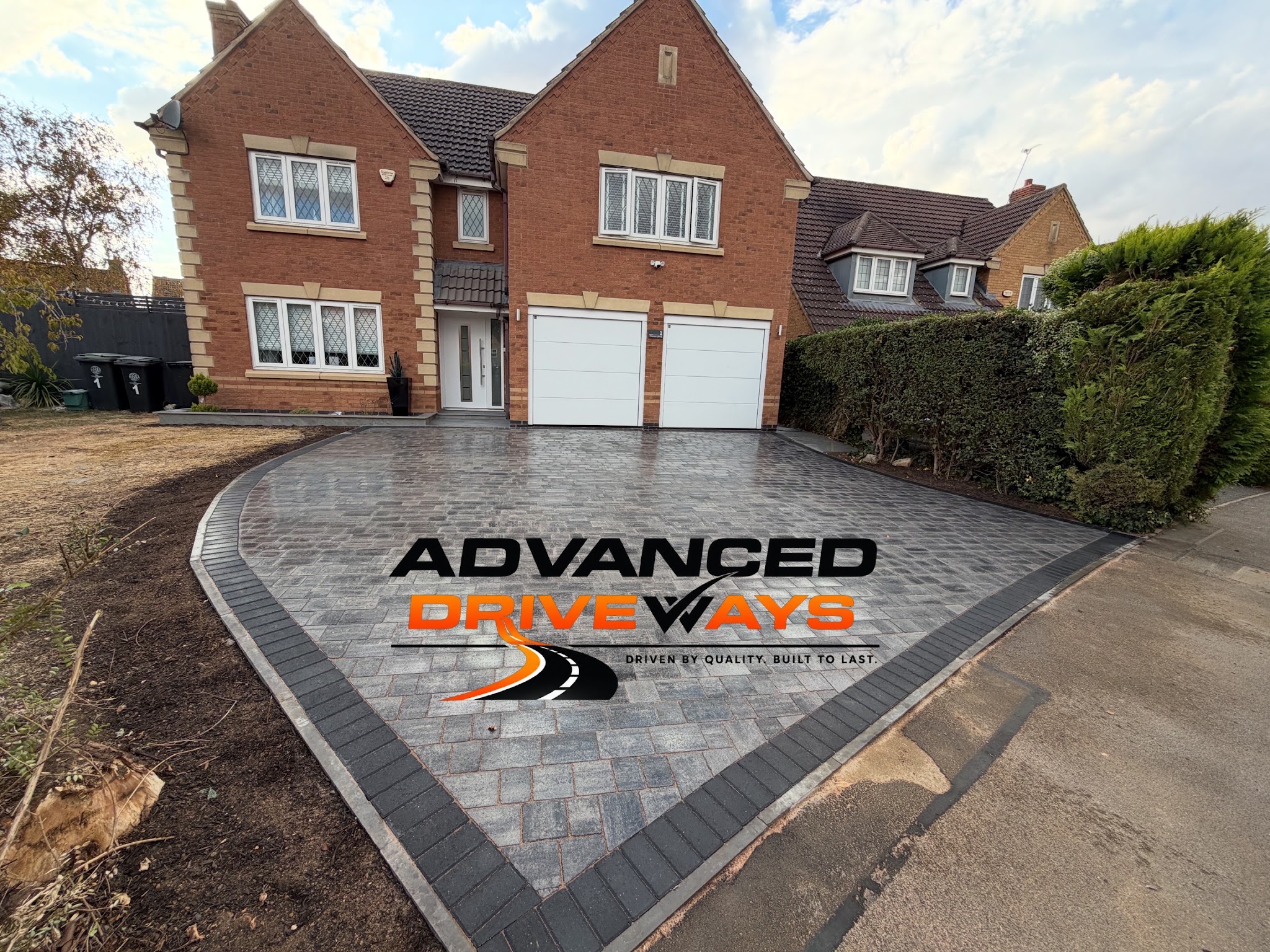 Large grey block-paved driveway with a charcoal border in front of a double garage