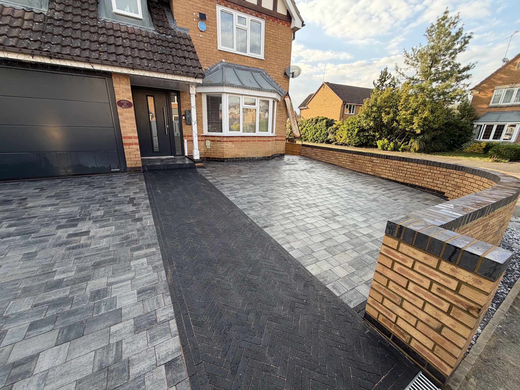 Grey block-paved driveway with a charcoal herringbone path and a new brick wall